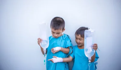 Two young boys in hospital gowns, both holding IV bags
