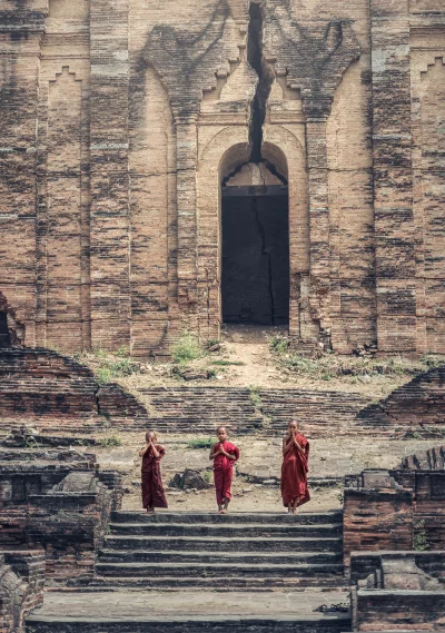 Three Buddhist monks in red robes standing in front of a temple