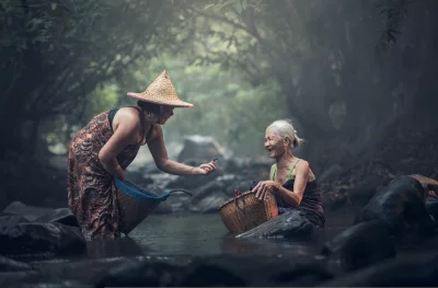 Two women standing in a river and both wearing traditional clothing and are carrying baskets