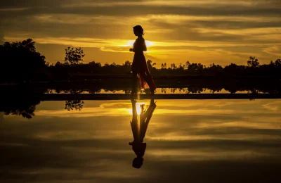 Girl walking on a beach at sunset sky is a bright orange, and the water is calm