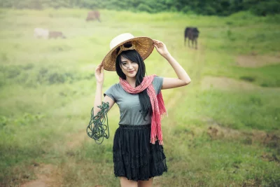 A woman standing in a field and wearing a traditional Vietnamese hat and a colorful scarf with roof