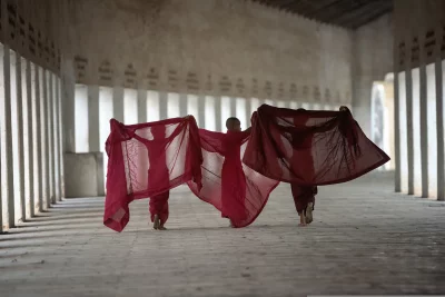 Three monks walking away from the camera and monks are wearing traditional robes are carrying their belongings in bundles on their backs