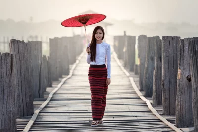 Burmese woman in traditional dress walking on a wooden bridge