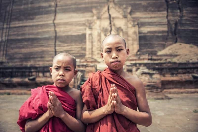 Two Buddhist monks standing in front of a temple and both wearing red robes and have their heads shaved