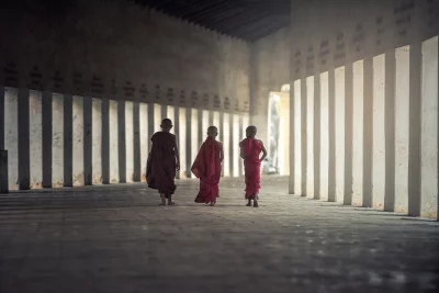 Three monks walking away from the camera and wearing traditional robes and are walking barefoot