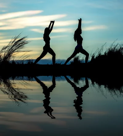 Two women doing yoga on a beach at sunset