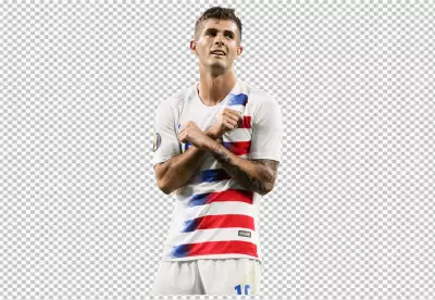 Christian Pulisic is standing with his arms crossed in front of his chest, looking off to the left