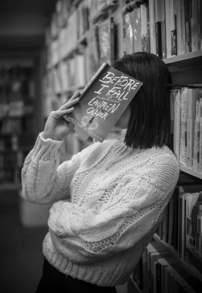 Woman Reading Book in Black and White Library Setting with Cozy Sweater