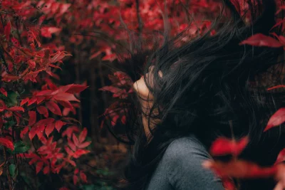 Dynamic Woman Tossing Long Dark Hair Amidst Vibrant Red Autumn Leaves image