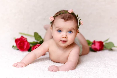 Adorable Infant with Blue Eyes and Pink Rose Headband Posing on Soft White Carpet image