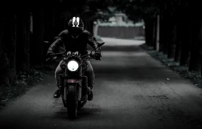 Motorcyclist on Dark Forest Road with Illuminated Headlight image