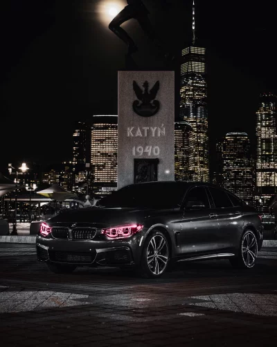 Sleek Black BMW Performance Car with Red Headlights and City Skyline at Night image