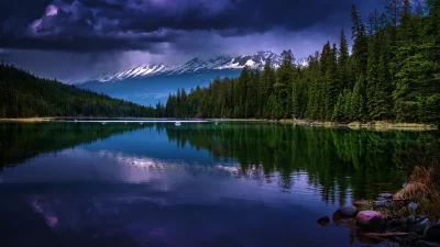 Dramatic Alpine Lake Reflection with Forest and Snow-Capped Mountains Under Dark Clouds image