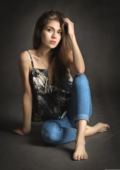 Pensive Young Woman in Floral Camisole and Jeans Sitting Barefoot image