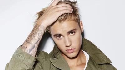 Confident Young Man with Stylish Blonde Hair and Arm Tattoo Posing in Green Jacket image