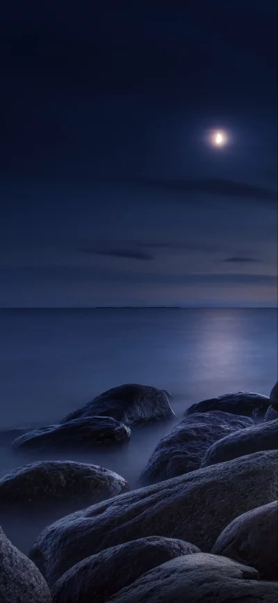 Moonlit Rocky Shoreline with Calm Ocean and Distant Horizon at Night