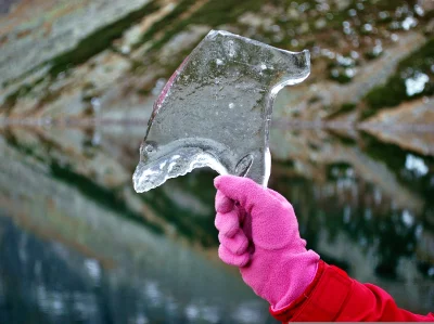 Vibrant Pink Gloved Hand Holding a Translucent Ice Shard in a Cold Winter Landscape image