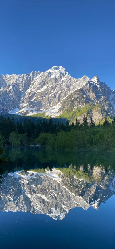 Snow-capped mountains reflected in a serene alpine lake under a clear blue sky.