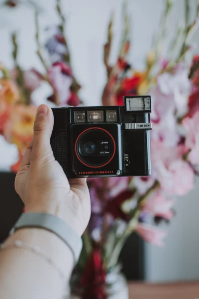 A person holding a black camera in front of a bouquet of flowers