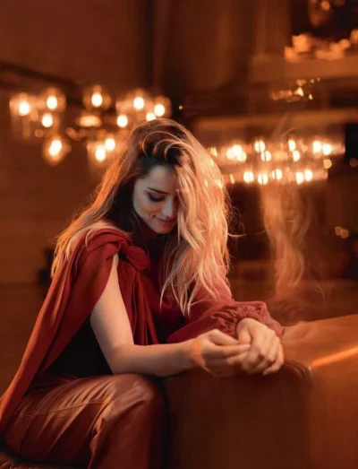 Elegant woman in a red outfit smiling indoors with warm bokeh lights in the background, creating a cozy atmosphere image