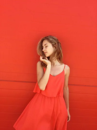 Young Woman Enjoys Sun in a Vibrant Orange Sundress Against Red Wall