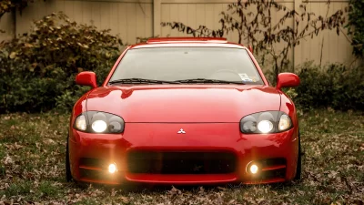 Vibrant Red Mitsubishi GTO Sports Car Parked on Autumnal Lawn with Headlights On image