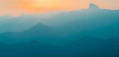 Misty Mountain Layers at Sunset with Vibrant Orange and Teal Sky image