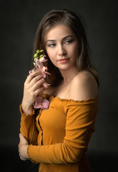 Young Woman in Orange Top Holding Pink Orchid with Thoughtful Gaze image