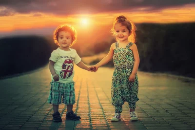 Young Boy and Girl Holding Hands Walking Towards Sunset on Cobblestone Road image