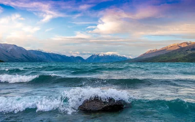 Majestic Snow-Capped Mountains Overlook Turbulent Waves on a Vast Lake Under a Colorful Sky image