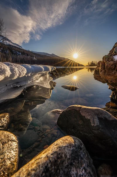 Breathtaking winter sunrise over a frozen lake with sunburst reflection