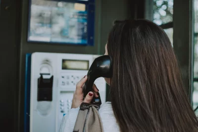 Woman is standing in a phone booth, and she is holding the phone to her ear