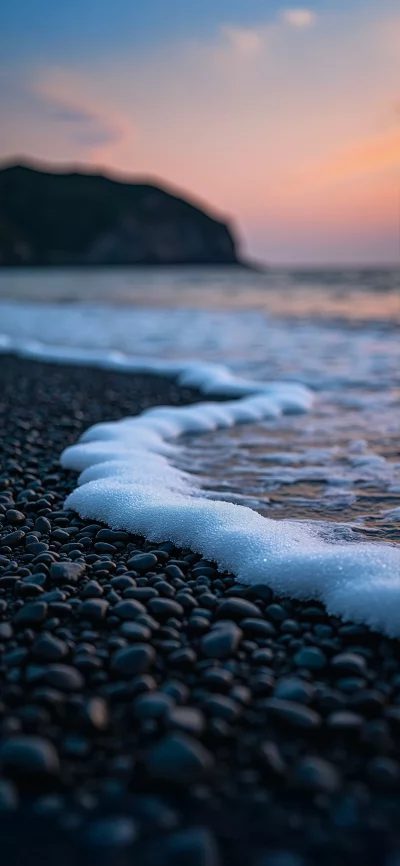 Serene view of foamy ocean waves rolling onto a dark stone beach at dusk image