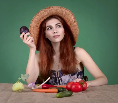 Thoughtful Young Woman in Straw Hat Holding Avocado with Fresh Vegetables image