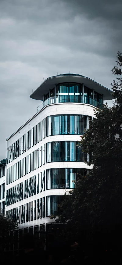 Modern white office building with curved facade and large windows under a cloudy sky