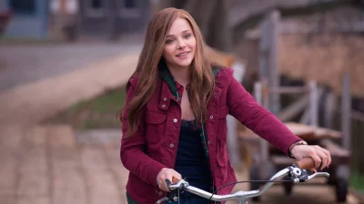 Smiling young woman with long hair and red jacket on a bicycle outdoors image