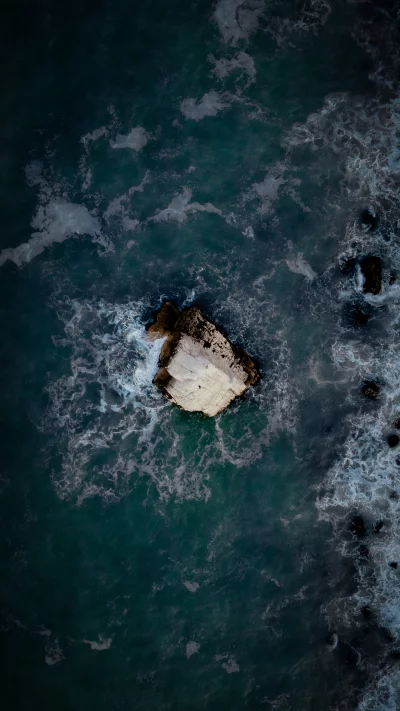 Aerial Perspective of a Massive Rock Formation in the Dark Ocean with Turbulent Waves image
