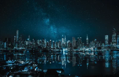 Vibrant City Skyline Illuminated Under a Star-Filled Night Sky with Water Reflections image