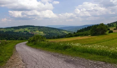 Winding Road Through Lush Green Mountain Landscape with Village and Cloudy Sky image