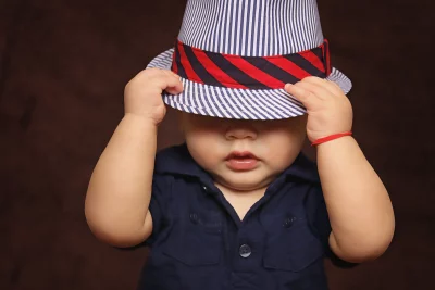 Playful Baby Peeking Under Striped Fedora Hat with Red Band image