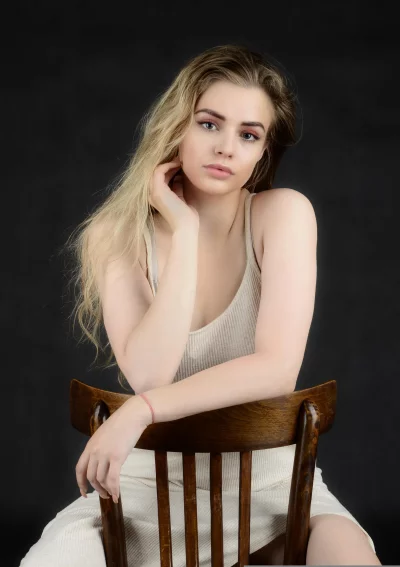 Young Blonde Woman Sitting on Wooden Chair in Contemplative Studio Portrait image