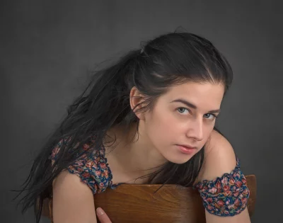 Young Woman Leaning on Chair with Pensive Gaze and Long Dark Hair image