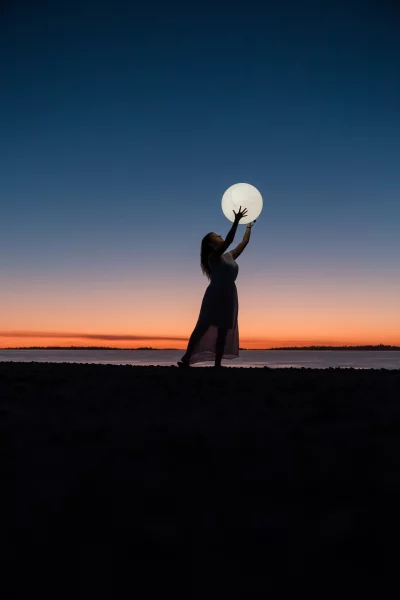 Ethereal Woman's Silhouette Holding Luminous Orb Against Vivid Sunset Sky image