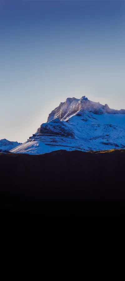 Snow-capped mountain summit bathed in golden sunlight under a clear blue sky