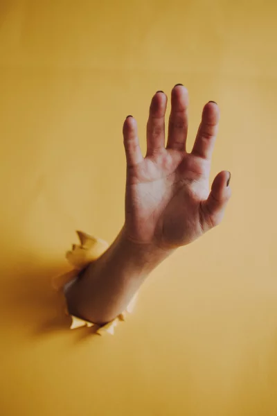 a hand reaching out from a hole in a yellow paper background