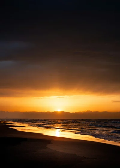 Dramatic sunset over ocean waves and sandy beach with reflection