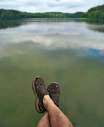 Relaxed Legs in Hiking Sandals Dangling Over Tranquil Lake with Forest Horizon image