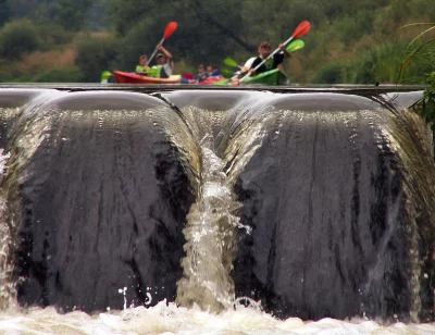 Group of Kayakers Navigating a River Weir with Splashing Water and Lush Green Background image