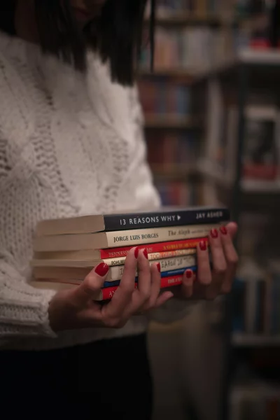 Hands holding stack of books with bright red nail polish