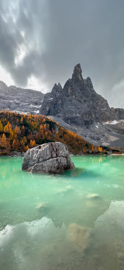 Dramatic mountain landscape reflected in turquoise lake with rocky boulder